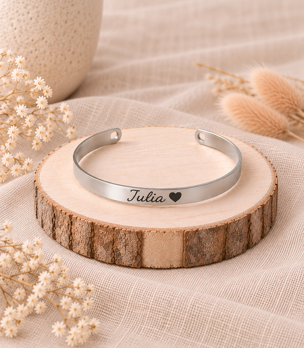 Brazalete rígido Imara plateado personalizado con nombre Julia y corazón grabado, sobre rodaja de madera con flores secas